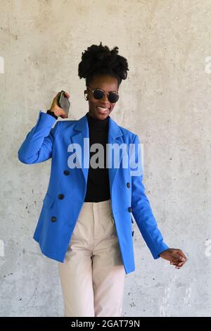 Femme africaine portant des écouteurs sans fil, dansant sur un mur de béton. Banque D'Images