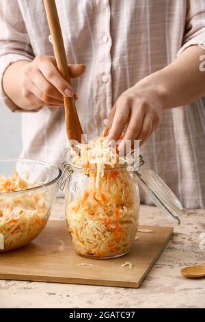 Femme mettant la choucroute savoureuse dans un pot en verre sur une table dans la cuisine, gros plan Banque D'Images