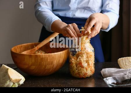 Femme mettant la choucroute savoureuse dans un pot en verre sur une table dans la cuisine, gros plan Banque D'Images