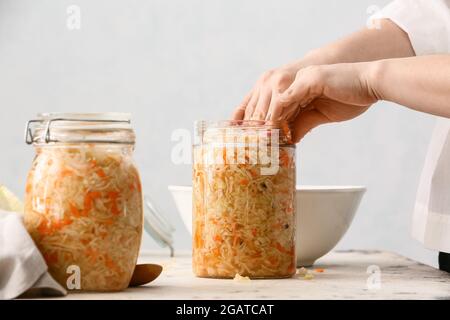 Femme mettant la choucroute savoureuse dans un pot en verre sur une table dans la cuisine, gros plan Banque D'Images