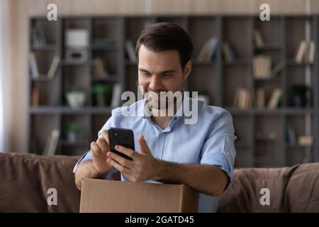 Un homme joyeux du millénaire utilisant un téléphone portable pour filmer le déballage Banque D'Images