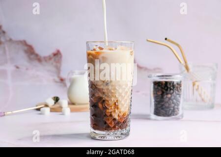 Verser le lait dans un verre de café chaud sur fond clair Banque D'Images
