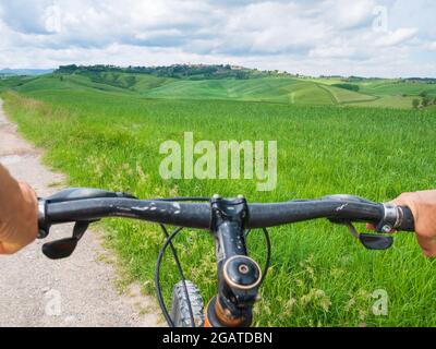 POV Mountain bike gros plan. Une personne qui fait du VTT sur la route de la terre parmi les champs cultivés. Paysage vert en Toscane, Italie. Banque D'Images