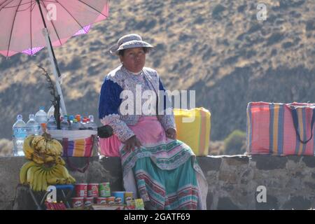 Dame avec parapluie dans le Canyon de Colca au Pérou dame assis vendant des bananes boissons nourriture et eau sur le mur avec parapluie et sac froid dans les montagnes Banque D'Images