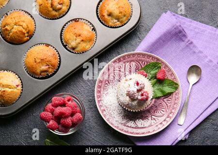 Assiette et broche de cuisson avec de savoureux muffins aux framboises sur fond sombre Banque D'Images