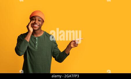 Regardez ceci. Happy Young African American Guy pointant de côté à Copy Space, gai Black Man gardant la main près de la bouche, recommandant Nice offre pendant Banque D'Images