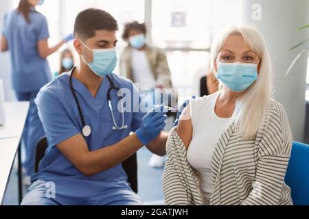 Vaccination Covid-19. Femme âgée se faire vacciner contre le coronavirus assis à l'hôpital avec un médecin, portant un masque facial. Médecin Injecti Banque D'Images