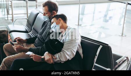 Homme et femme voyageur pendant une pandémie assis au terminal de l'aéroport. Couple de passagers portant un masque facial en attente d'un vol retardé. Banque D'Images