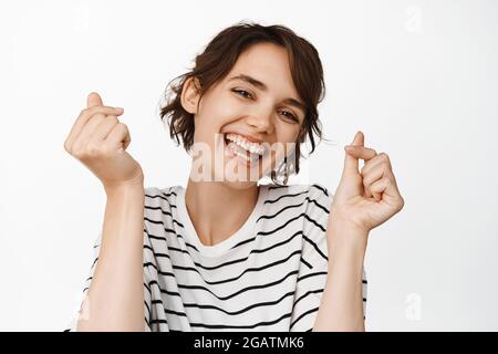 Portrait en gros plan de la femme heureuse brunette, danse et rire, dents blanches souriantes, debout dans le tee-shirt sur fond blanc Banque D'Images