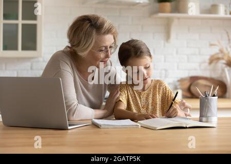 Une grand-mère attentionnée dans des verres aidant la petite petite-fille à faire ses devoirs à l'école Banque D'Images