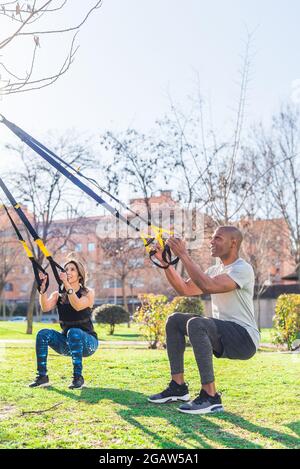 Couple de forme physique faire des jambes exercice avec trx sangles de forme physique dans le parc Banque D'Images