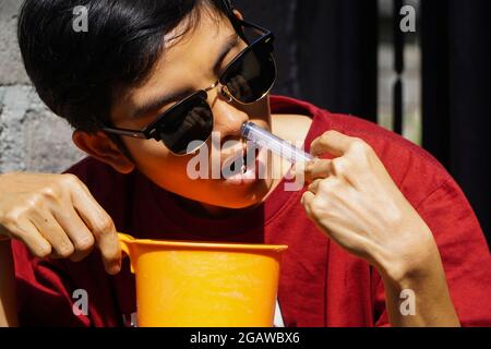 Une femme aux cheveux courts portant des lunettes de soleil et une chemise rouge, utilise une seringue pour injecter du liquide NaCl dans son nez pour nettoyer son nez des germes, la maladie Banque D'Images