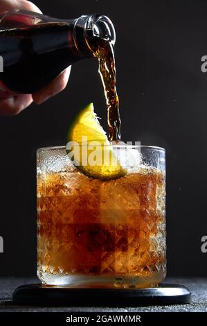 Cuba libre ou long Island cocktail avec verser le cola, le rhum et la chaux dans le verre sur fond sombre. Boisson rafraîchissante d'été. Banque D'Images