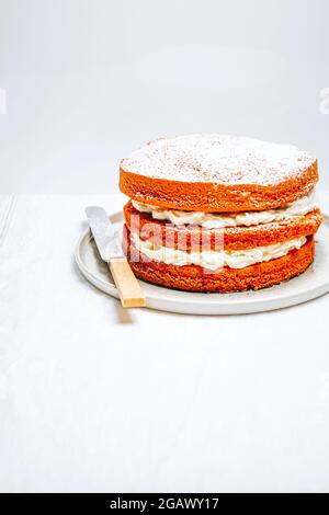 Victoria Sponge Cake fourré de crème fouettée sur une assiette avec un couteau sur une table – blanc FOOPPIX, COPYSPACE Banque D'Images