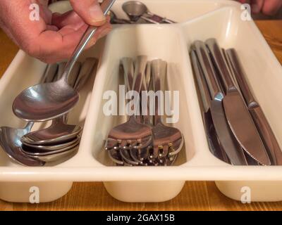Gros plan de la main d’un homme en plaçant une cuillère sur les autres dans un plateau à couverts en plastique, avec des compartiments pour couteaux en acier, fourchettes et cuillères. Banque D'Images