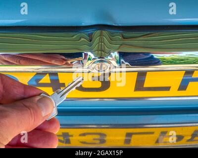 Gros plan de la main d'un homme sur le point de mettre une clé dans le coffre/coffre en chrome poli, pour verrouiller ou déverrouiller une vieille voiture Jaguar classique. Banque D'Images