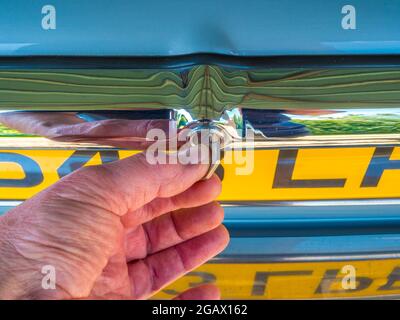 Gros plan de la main d'un homme tournant une clé dans un coffre/coffre chromé poli, pour verrouiller ou déverrouiller une vieille voiture Jaguar classique. Banque D'Images