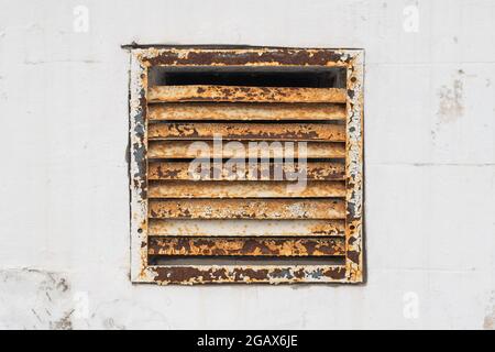 Grille de ventilation en fer rouillé peinte en blanc intégrée dans un mur peint en blanc composé de blocs de pierre Banque D'Images