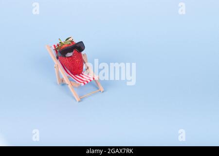 Idée créative faite de chaise de pont, parasol et fraise avec lunettes de soleil sur un fond bleu pastel. Concept de vacances d'été minimum. Banque D'Images