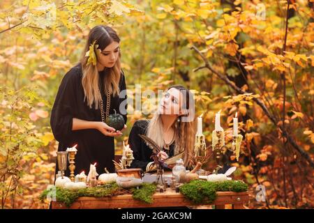 Jeunes femmes en costumes de sorcière assis à table avec des ingrédients magiques le jour d'automne dans la forêt Banque D'Images