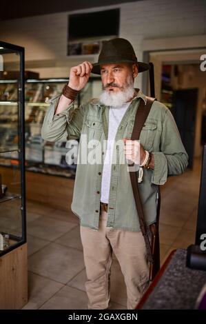 Un chasseur mâle barbu essaie de se faire un chapeau dans un magasin d'armes à feu Banque D'Images