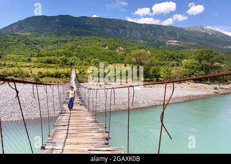 Une femme touriste traversant ancien pont suspendu au-dessus de la belle rivière Vjosa, près de Çarçovë, montagnes Nemërçka, district de Gjirokastra, albanie Banque D'Images