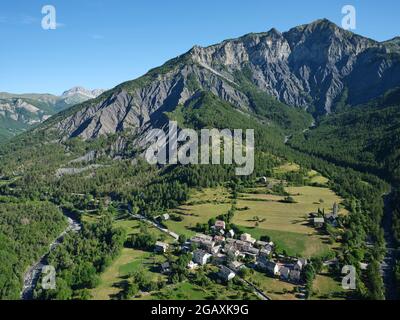 VUE AÉRIENNE. Village de Villeneuve d'Entraunes au pied d'une montagne rocheuse dans la haute vallée du Var. Alpes-Maritimes, France. Banque D'Images