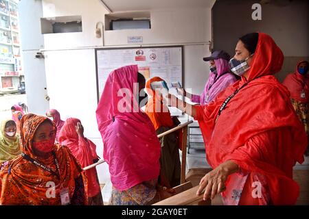 Le personnel de sécurité vérifie la température corporelle des travailleurs de l'habillement avant d'entrer dans une usine de vêtements après la réouverture des usines de vêtements pendant le confinement de Covid-19 à Dhaka, au Bangladesh, le 1er août 2021. Banque D'Images