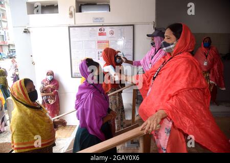 Le personnel de sécurité vérifie la température corporelle des travailleurs de l'habillement avant d'entrer dans une usine de vêtements après la réouverture des usines de vêtements pendant le confinement de Covid-19 à Dhaka, au Bangladesh, le 1er août 2021. Banque D'Images