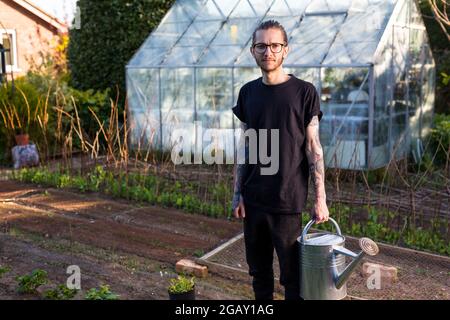 Woodbridge Suffolk Royaume-Uni Mai 08 2020: Un jeune homme tatoué hipster travaillant fièrement dans son jardin potager cultivant une gamme de légumes biologiques Banque D'Images