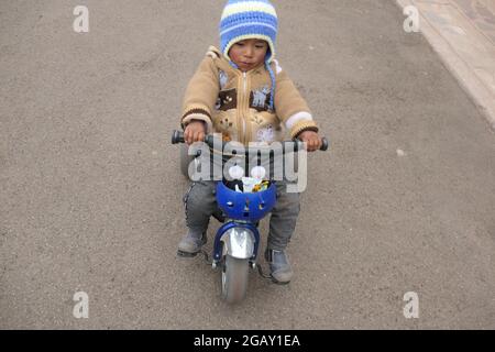 Enfant à vélo au Pérou avec chapeau et manteau par temps froid style moto type bébé enfant jouer à l'extérieur chemin casque jouer à des jeux conception de jeu Banque D'Images