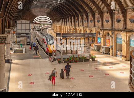 Un hall de gare avec un panneau d'affichage électronique de la gare et un train en attente de départ. Les passagers sont sur la plate-forme et un 19ème Centu élaboré Banque D'Images