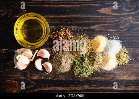 Ingrédients pour le pain italien huile à tremper sur une table en bois : épices séchées, gousses d'ail et huile d'olive extra vierge sur fond de bois foncé Banque D'Images