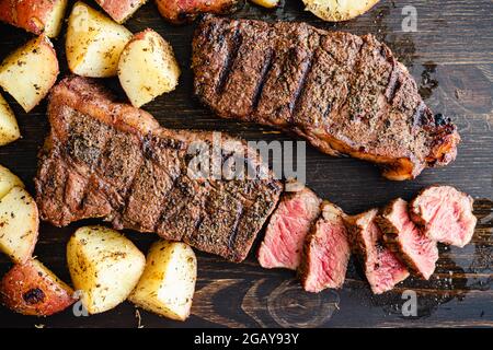 Steak de New York grillé avec café et pommes de terre rôties : biftecks de New York grillés avec pommes de terre rôties sur fond de bois sombre Banque D'Images