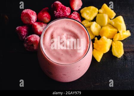 Smoothie aux ananas aux fraises avec fruits congelés à l'arrière-plan : un smoothy rose avec des fraises congelées et des morceaux d'ananas Banque D'Images