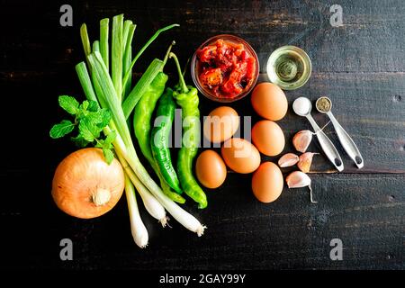 Ingrédients de meneurs turcs sur fond de bois foncé : œufs non cuits, tomates en dés, légumes et épices sur une table en bois Banque D'Images