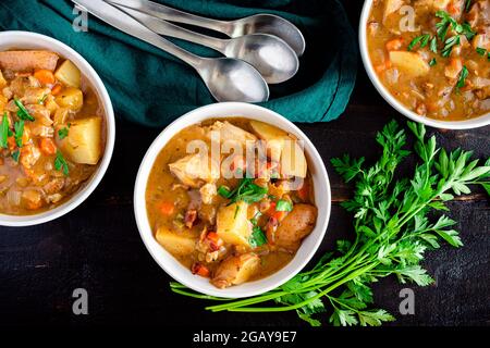 Ragoût de poulet avec pommes de terre et carottes dans un bouillon de vin blanc : bols de vin blanc frais ragoût de poulet garni de persil haché Banque D'Images