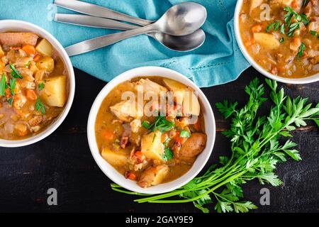 Ragoût de poulet avec pommes de terre et carottes dans un bouillon de vin blanc : bols de vin blanc frais ragoût de poulet garni de persil haché Banque D'Images