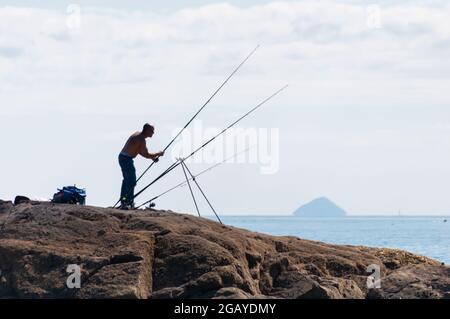 Portencross, Écosse, Royaume-Uni. 1er août 2021. Météo au Royaume-Uni : un homme pêchant sur la rive avec Ailsa Craig à l'horizon. Credit: SKULLY/Alay Live News Banque D'Images