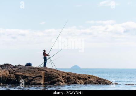 Portencross, Écosse, Royaume-Uni. 1er août 2021. Météo au Royaume-Uni : un homme pêchant sur la rive avec Ailsa Craig à l'horizon. Credit: SKULLY/Alay Live News Banque D'Images