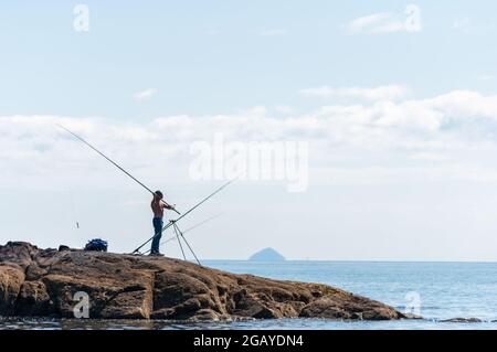 Portencross, Écosse, Royaume-Uni. 1er août 2021. Météo au Royaume-Uni : un homme pêchant sur la rive avec Ailsa Craig à l'horizon. Credit: SKULLY/Alay Live News Banque D'Images