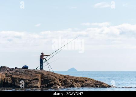 Portencross, Écosse, Royaume-Uni. 1er août 2021. Météo au Royaume-Uni : un homme pêchant sur la rive avec Ailsa Craig à l'horizon. Credit: SKULLY/Alay Live News Banque D'Images