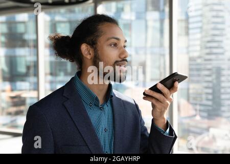 Jeune homme concentré responsable africain enregistrant un message audio. Banque D'Images