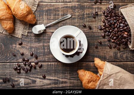Espresso dans une tasse blanche, cubes de sucre, grains de café, croissants frais sur fond de bois. Le concept d'un café-restaurant, le petit déjeuner traditionnel Banque D'Images