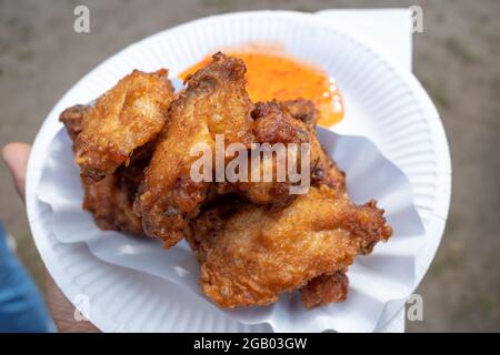 Tenez à la main le poulet frit de style asiatique et la sauce aigre-douce épicée sur une assiette en papier blanc. Banque D'Images