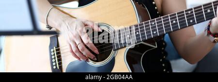 Mains de femmes tenant la guitare acoustique occidentale assis sur le canapé à la maison Banque D'Images