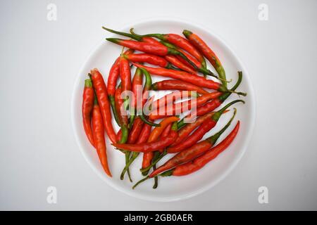 Les piments verts frais sont transformés en piments rouges mûrs avec tige verte. Les produits frais crus non séchés sont placés dans une plaque blanche avec un fond blanc. Chaud Indien asi Banque D'Images