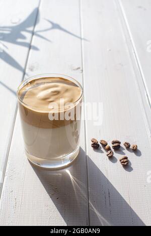 Boisson traditionnelle coréenne avec de la caféine, le café Dalgona dans un verre transparent avec des grains de café sur fond de tableaux blancs. Lait avec fouetté Banque D'Images