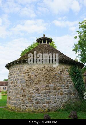 Un pigeonnier circulaire classé de grade II historique avec des murs en pierre caoutchoutée avec une coupole ouverte et un toit conique en pierre-ardoise Banque D'Images