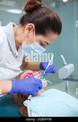 Prise de vue verticale d'une femme dentiste portant un masque médical, travaillant avec un enfant Banque D'Images